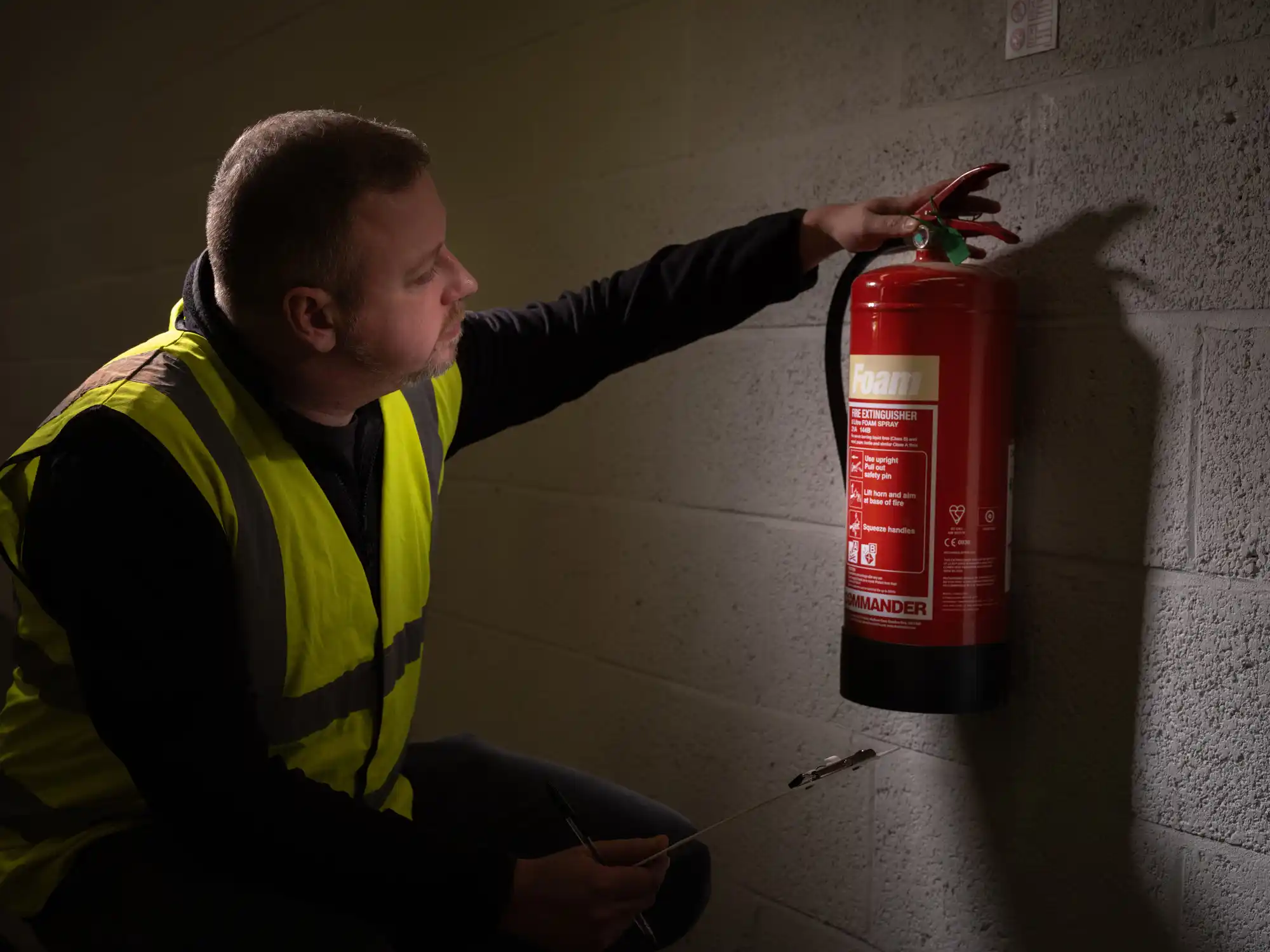 Adult male carrying out a fire safety inspection with clipboard including fire extinguisher visual inspection