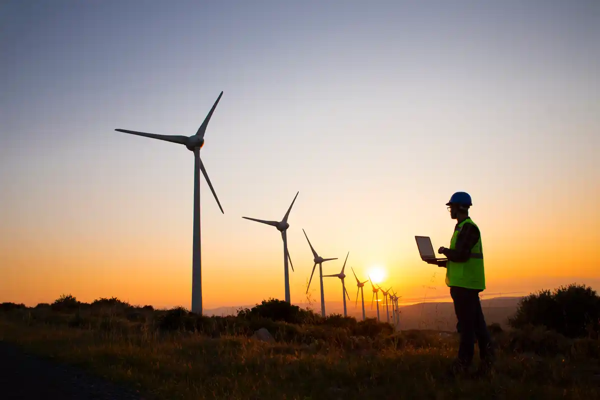 Engineer looking at wind farm with laptop
