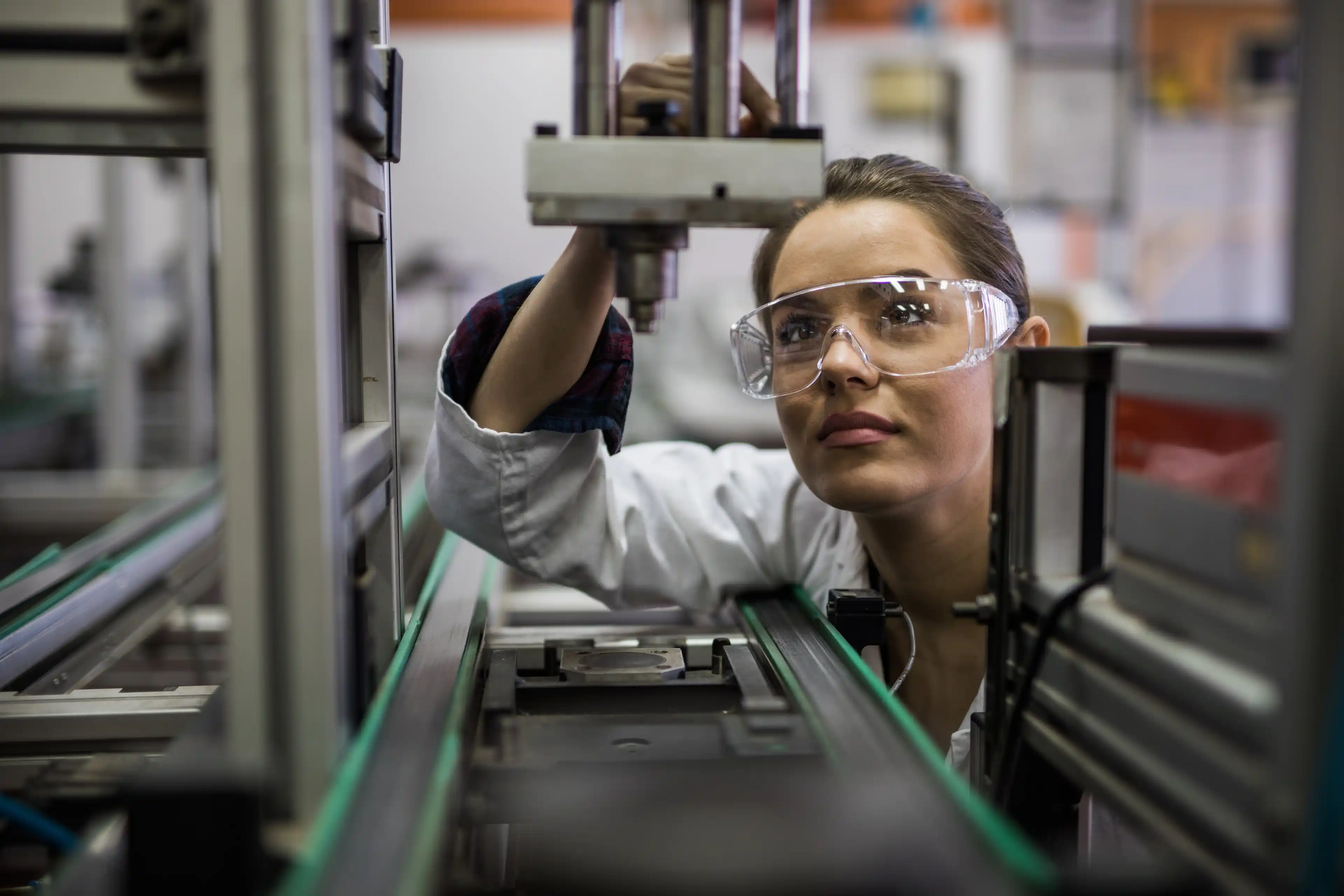 A worker wearing a lab coat and protective eyewear examines a machine