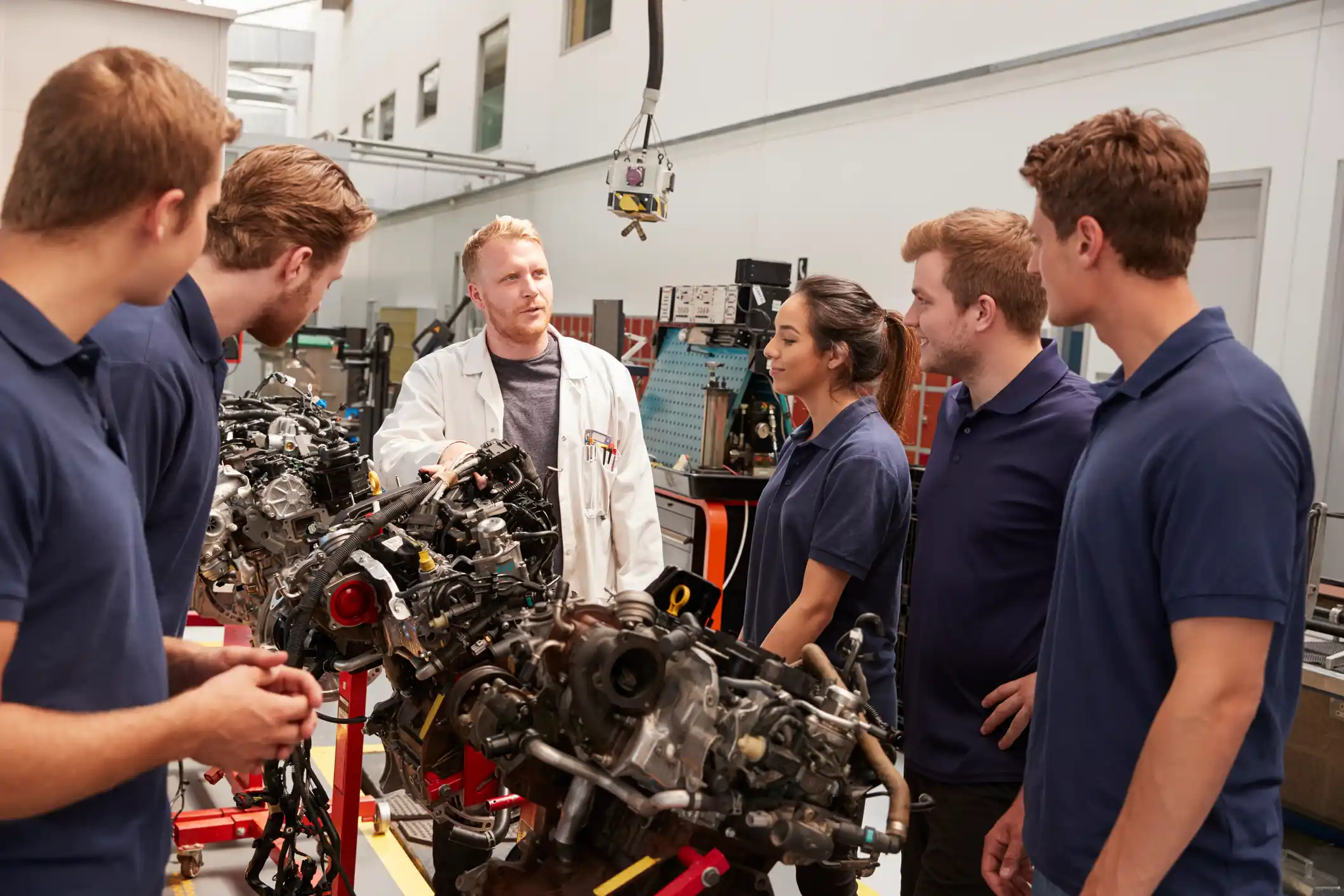 a white-coated technician leading a group of workshop apprentices