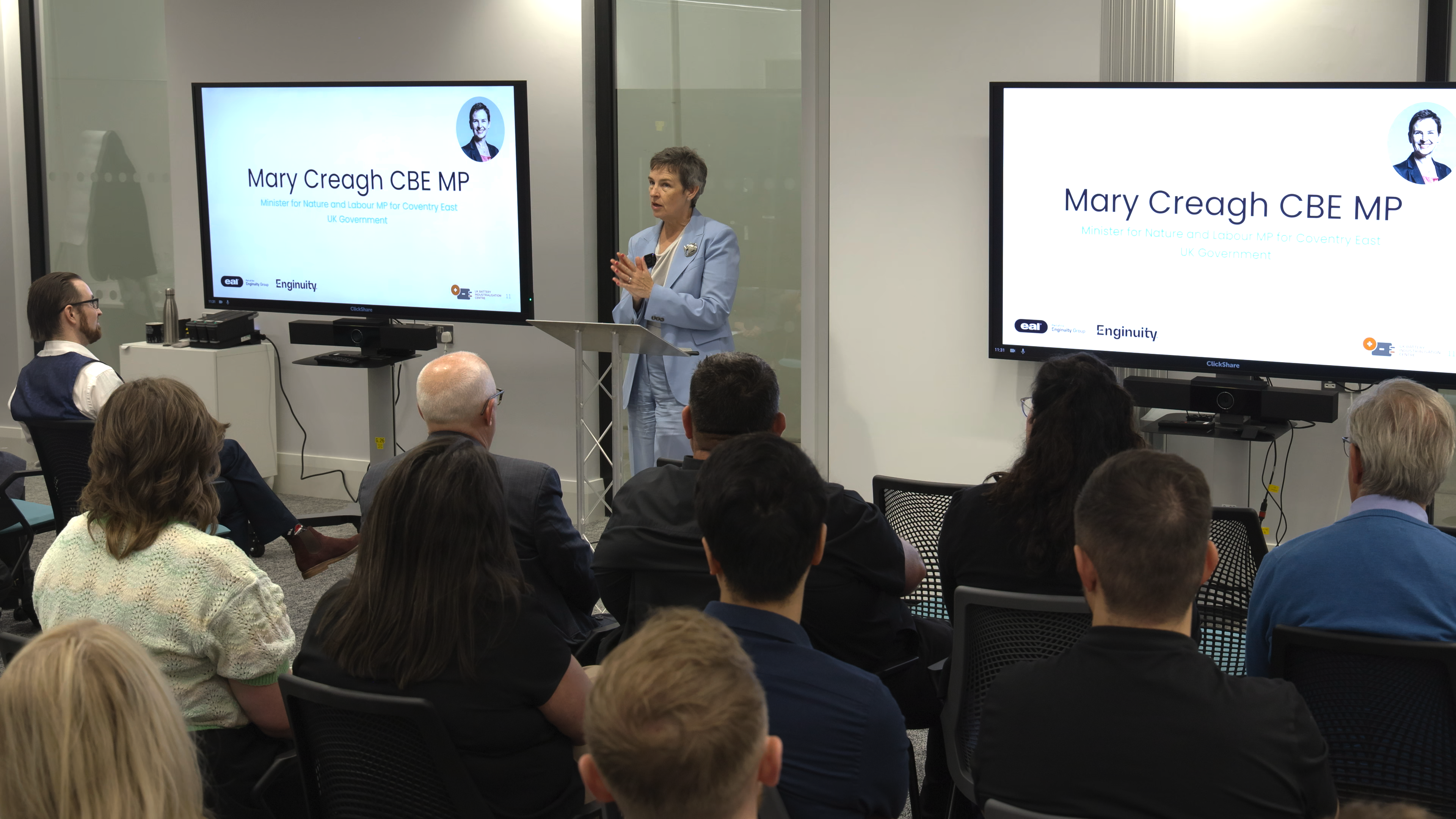 A woman in a light blue suit addresses an audience