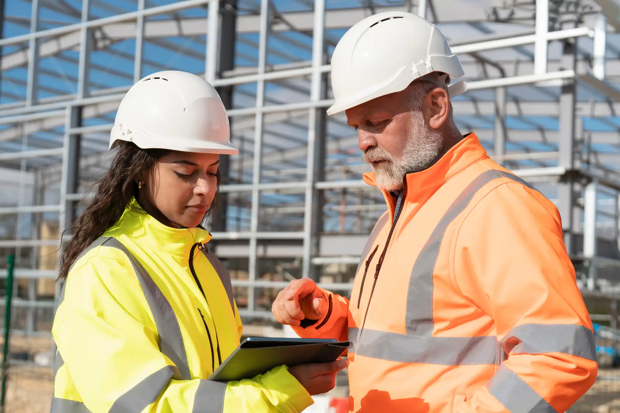 two engineers in protective hi-vis clothing on a construction site looking at a tablet