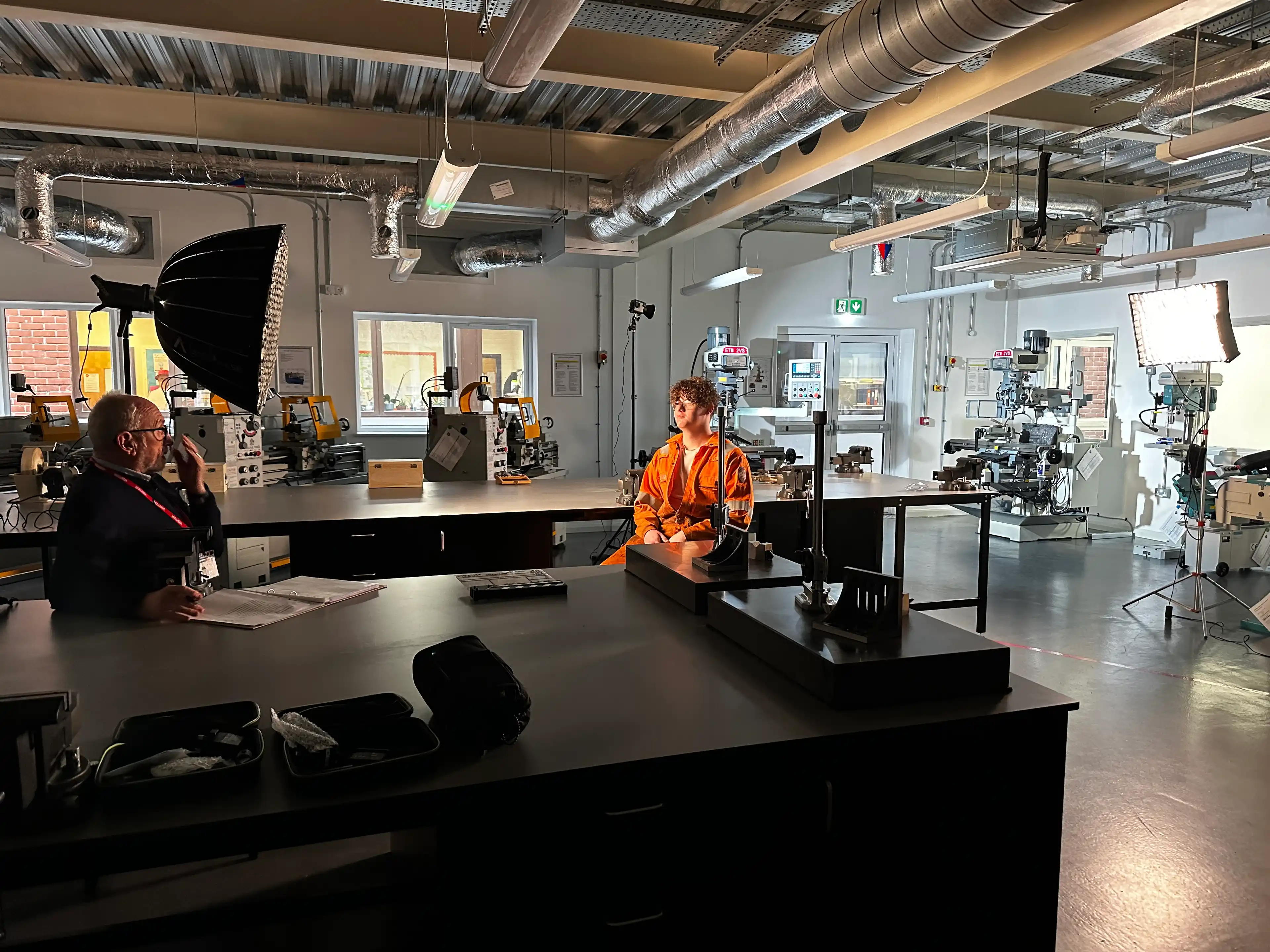 Jack Matthews in engineering lab being filmed in an orange high vis jacket.