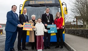 This is a photo opportunity for the launch of a new Sligo Town Route S3 bus route, with local officials and community representative. It is an eye-level view of a group of people standing in front of a yellow and blue Bus Éireann bus. 