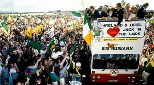 Outdoor shot of a large crowd of Irish Football supporters, cheering and waving flags welcoming the Irish Team home from Italia 90 who are aboard a Bus Éireann open top bus.
The words "IRELAND & OPEL JACK 'N' THE LADS", is prominently displayed in the center of the bus which is adorned with Irish flags and other patriotic symbols.