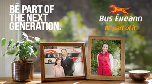 The image is a part of a recruitment campaign for Bus Éireann. The central focus is on a windowsill where two framed photographs are prominently displayed. The first photo shows a man in a suit and a young girl, standing in front of a Bus Éireann bus. The man is the grandfather of the girl; he has his arm around her. The second photo shows the same girl from the first photo, but now older, wearing a red Bus Éireann uniform jacket.