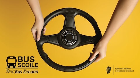 A close-up image features a black steering wheel held by two hands against a bright yellow background.