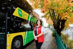 Image of female driver standing in from of yellow and green bus with 187 on its scroll