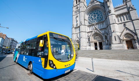 A blue and yellow Bus Éireann bus operating Route 173 is parked on a city street in front of a St Peters Cathedral in Drogheda.