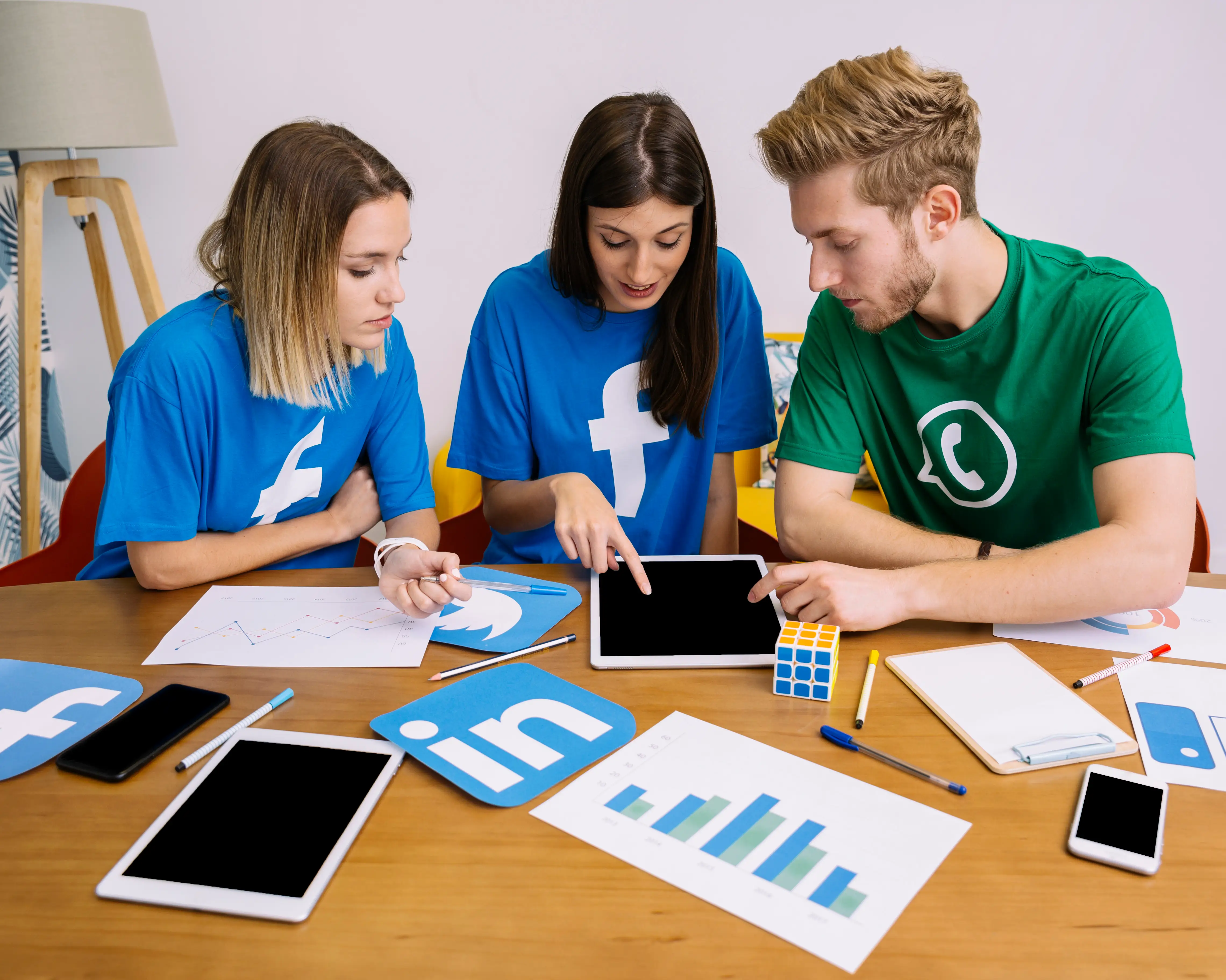 Equipo de redes sociales (Facebook y WhatsApp) trabajando en una mesa con tablets, cuadernos y gráficos de impresos.