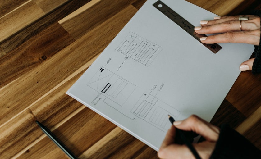 A person uses a ruler and pensil to draw on a white page