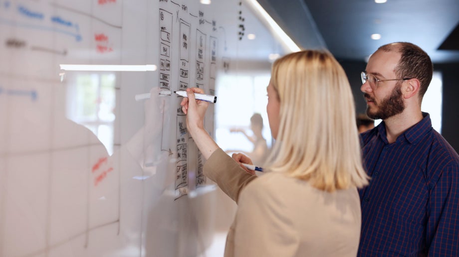 Two designers figuring out a problem on a whiteboard.