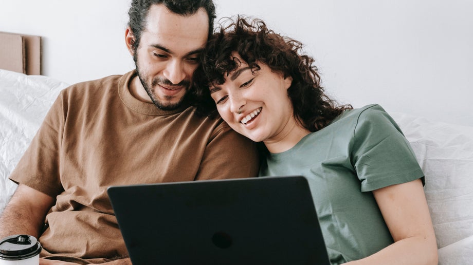 A couple sitting on the couch are looking at the laptop screen.