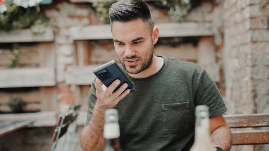 An individual is sitting outside and they have their mobile lifted up to their face to talk into their device.