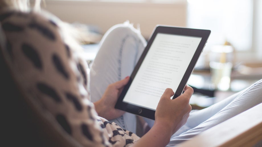 An individual is reading from their tablet screen while sitting in their home.