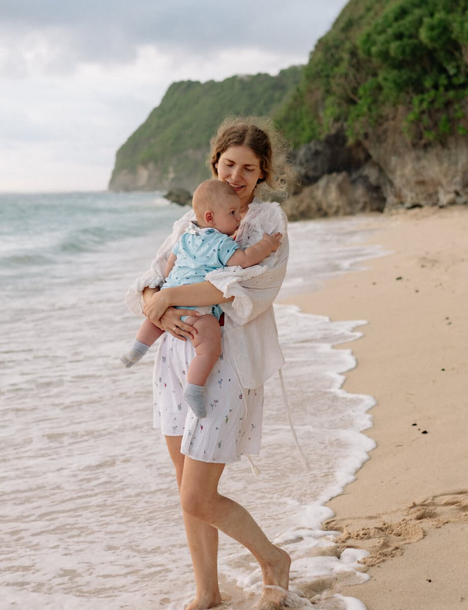 A woman walking on the beach is hugging her baby 