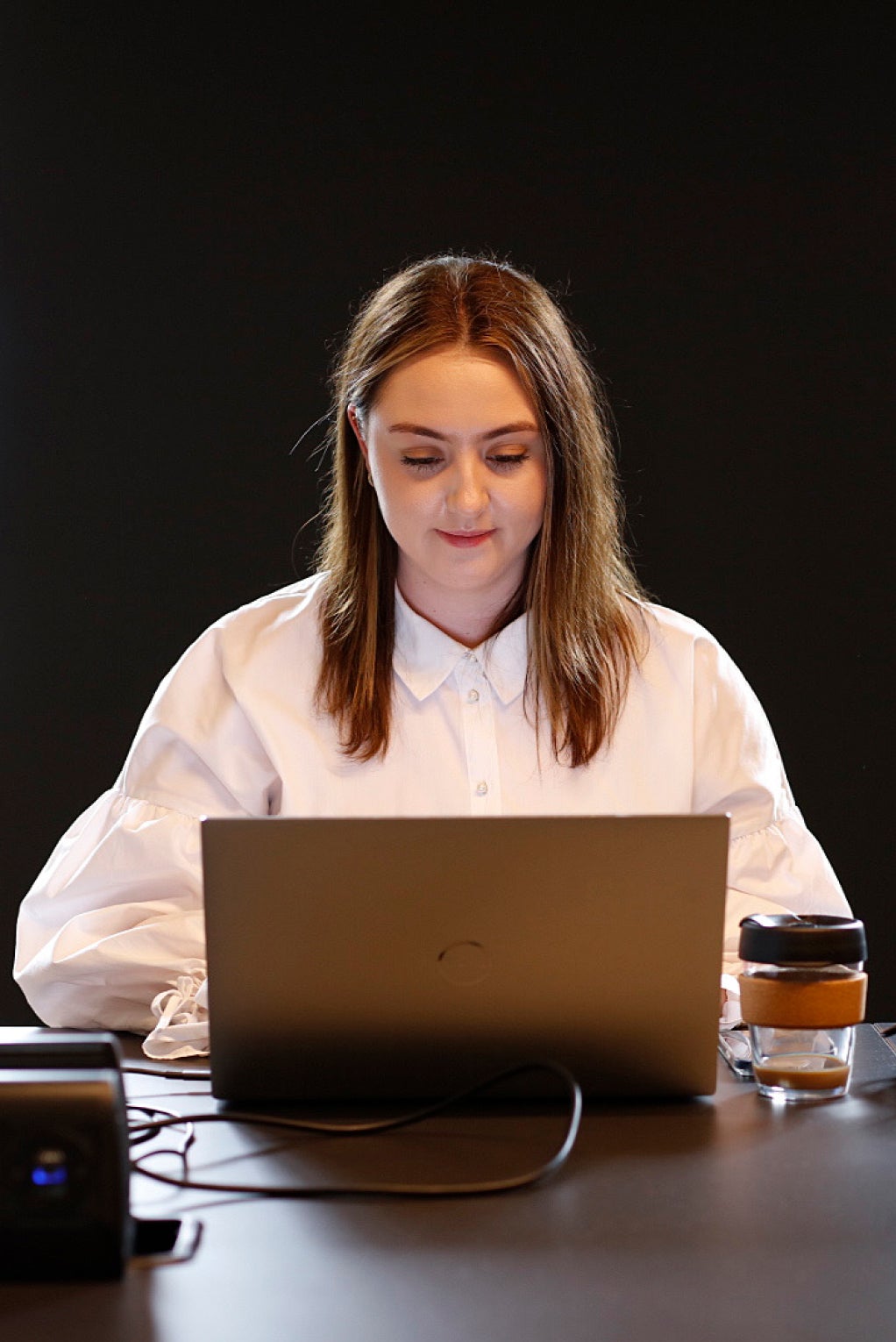 An individual in a smart white shirt is sitting down at a desk and working on their laptop in front of them. 