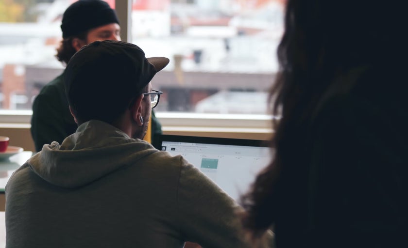 A person wearing a cap working on a laptop 