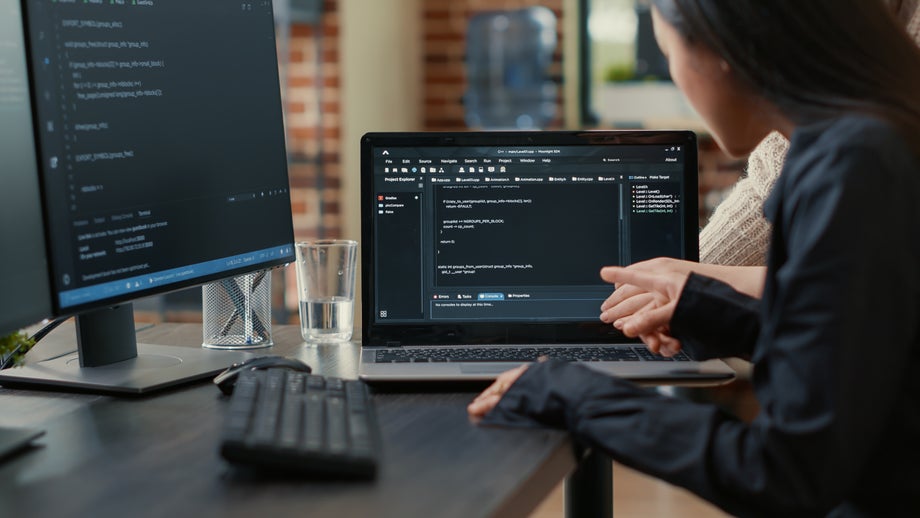 Person sitting at 2 computers working on a programming software