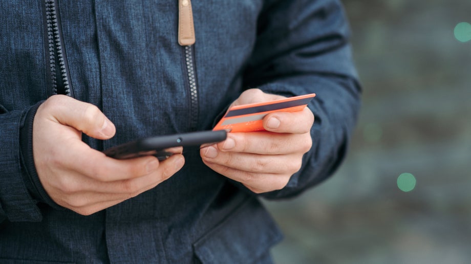A closeup of an individual outside using their mobile phone in one hand and holding a credit card in the other.