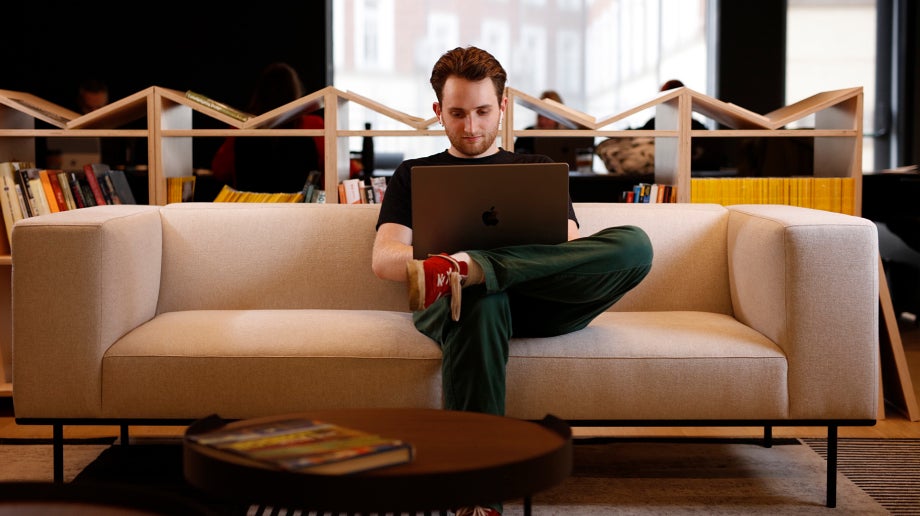 A man in the office sitting on the couch while working on his laptop