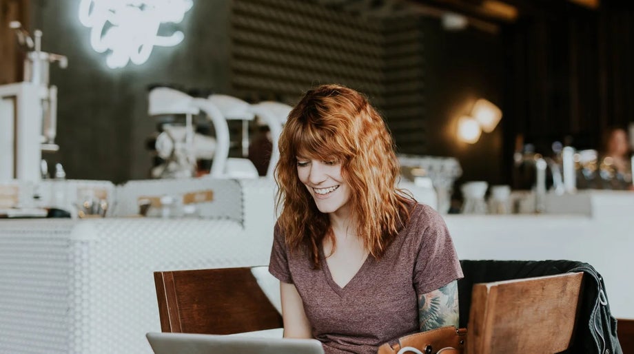 A person smiles while using their laptop in a cafe