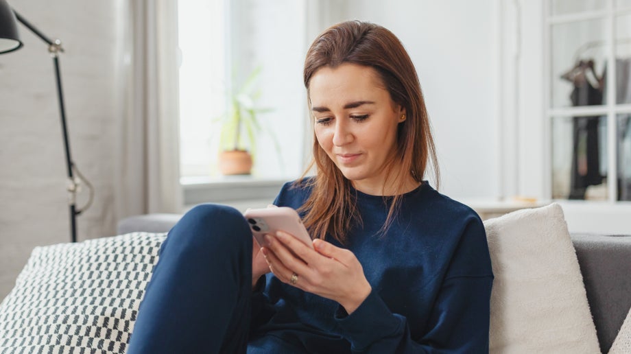 An individual is sitting down on the couch and looking at their mobile phone.