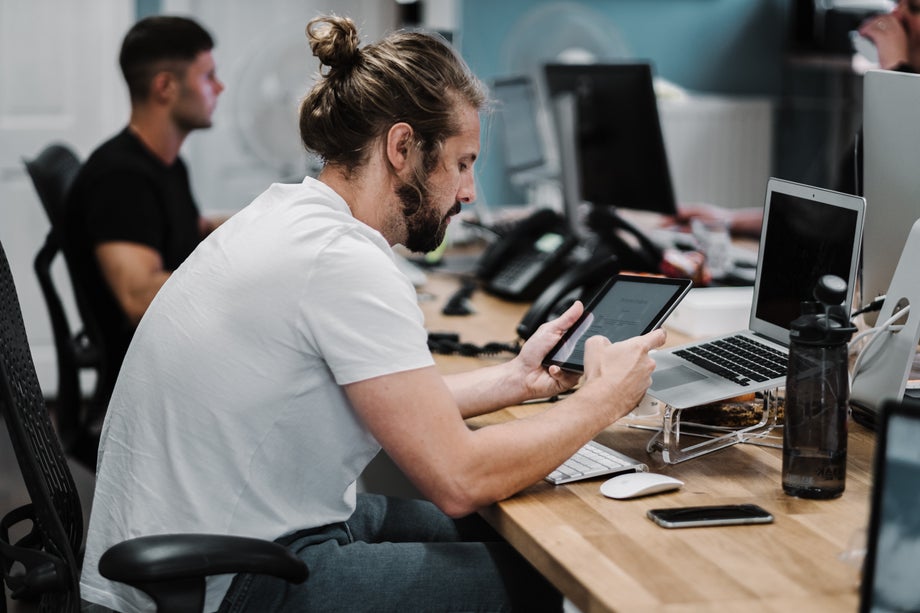 Man in front of multiple screens and looking at a device