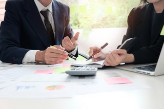 two people at a table with calculator and laptop