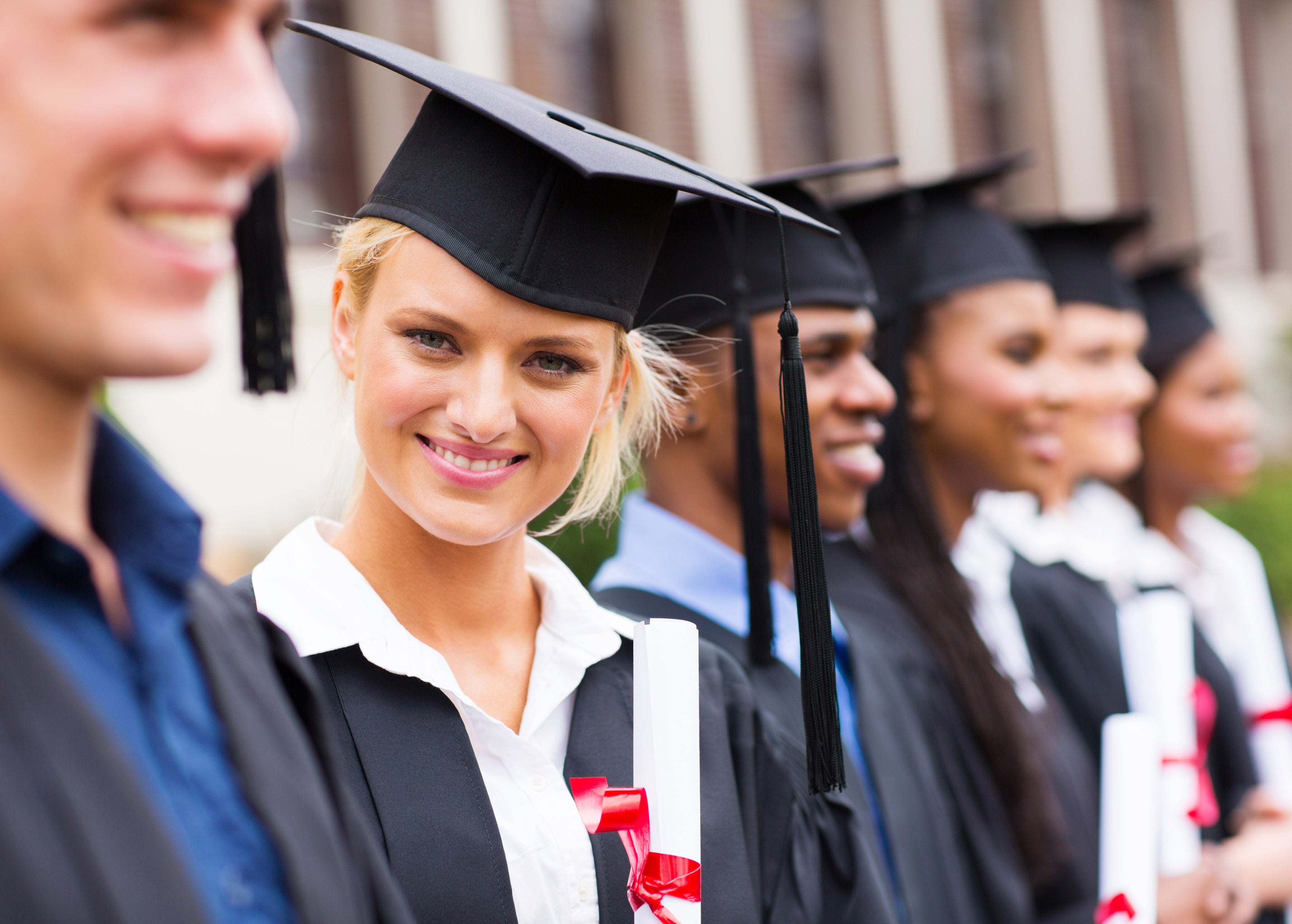 Woman in graduation cap smiles while holding diploma