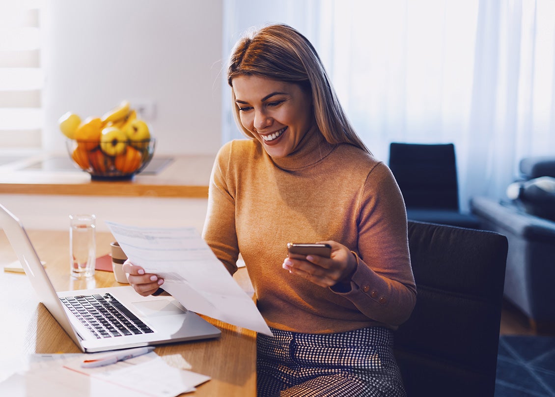 Woman sitting at desk with laptop while reviewing a spreadsheet