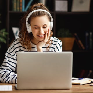 Woman wearing headphones smiles at laptop