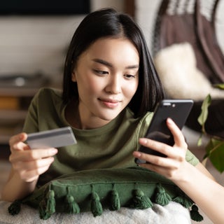 Young woman looks at phone with card in hand