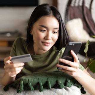 Young woman looks at phone with card in hand