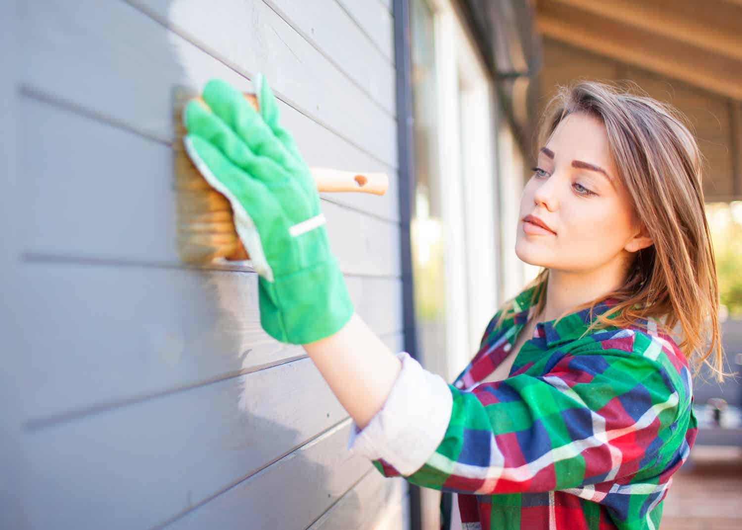 Woman paints house blue with paintbrush