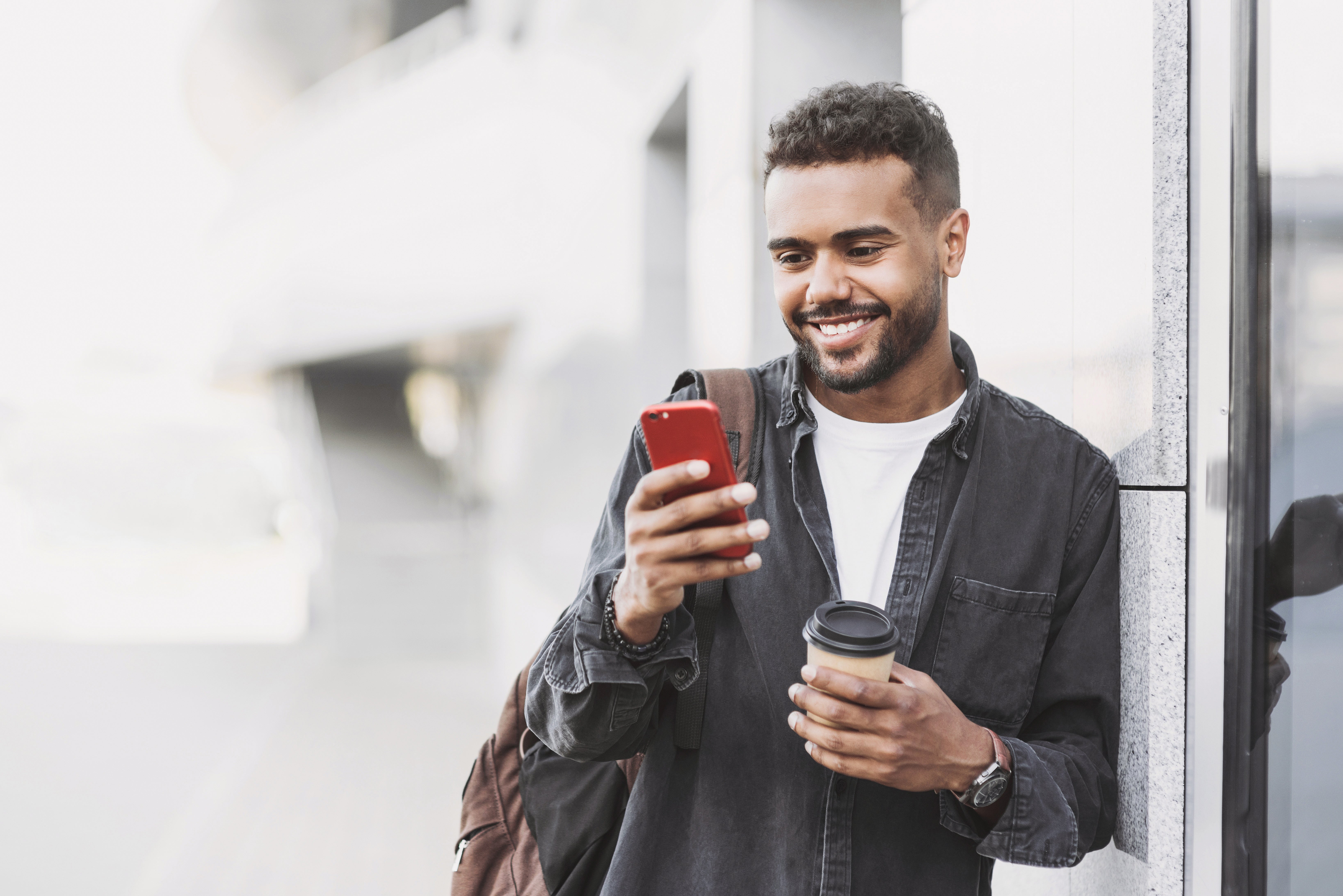 Man checks phone and smiles while holding coffee