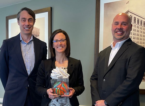 Employee holds excellence award next to management team