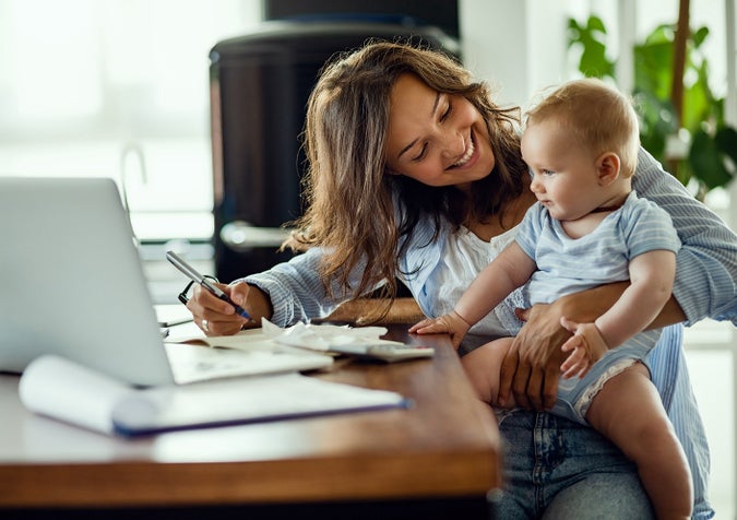 Mother and baby sit at desk working on laptop