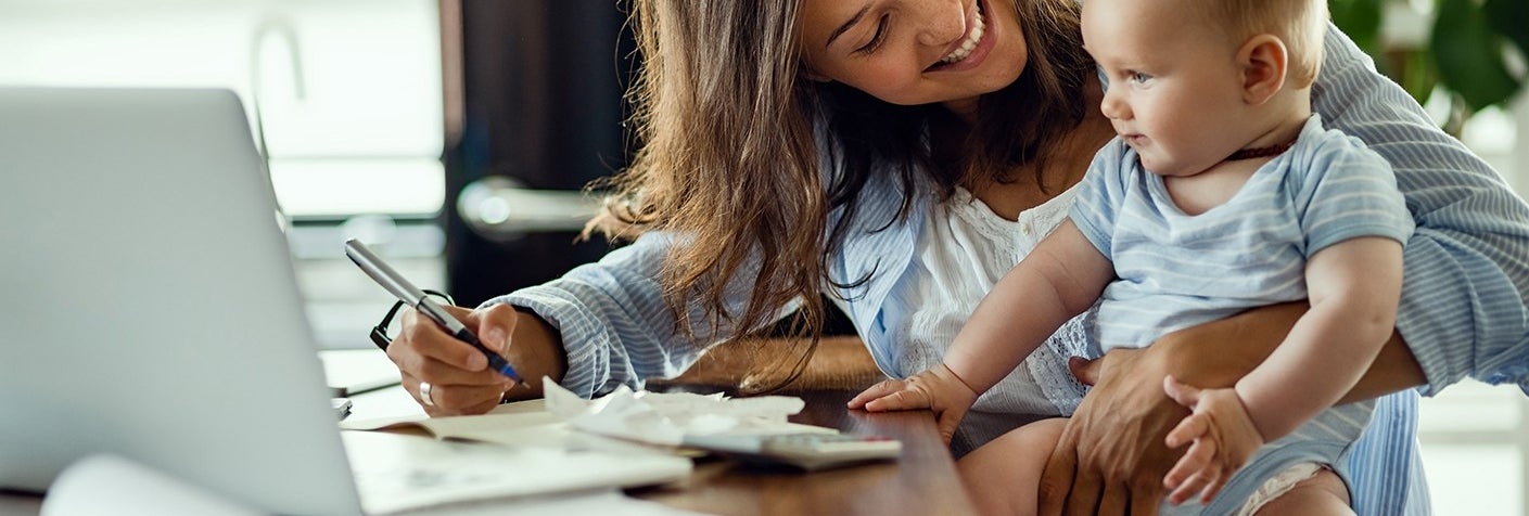 Mother and baby sit at desk working on laptop