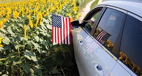 Car driving through sunflower field with USA flag