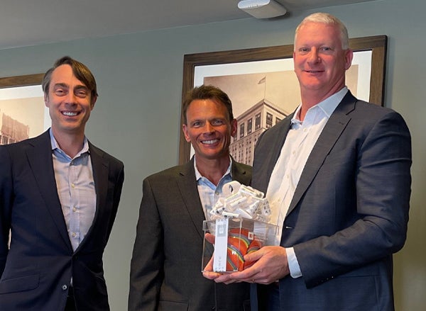 Employee holds excellence award next to management team