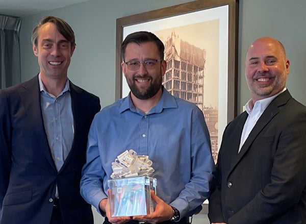Employee holds excellence award next to management team