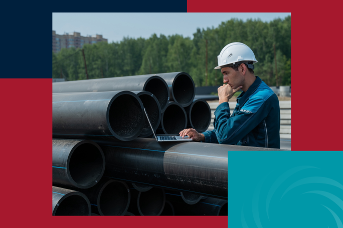 A man wearing a white hard hat and blue work uniform inspects a stack of large black pipes while working on a laptop. The background shows a green forested area and buildings in the distance. The image is framed with red and blue graphic design elements.