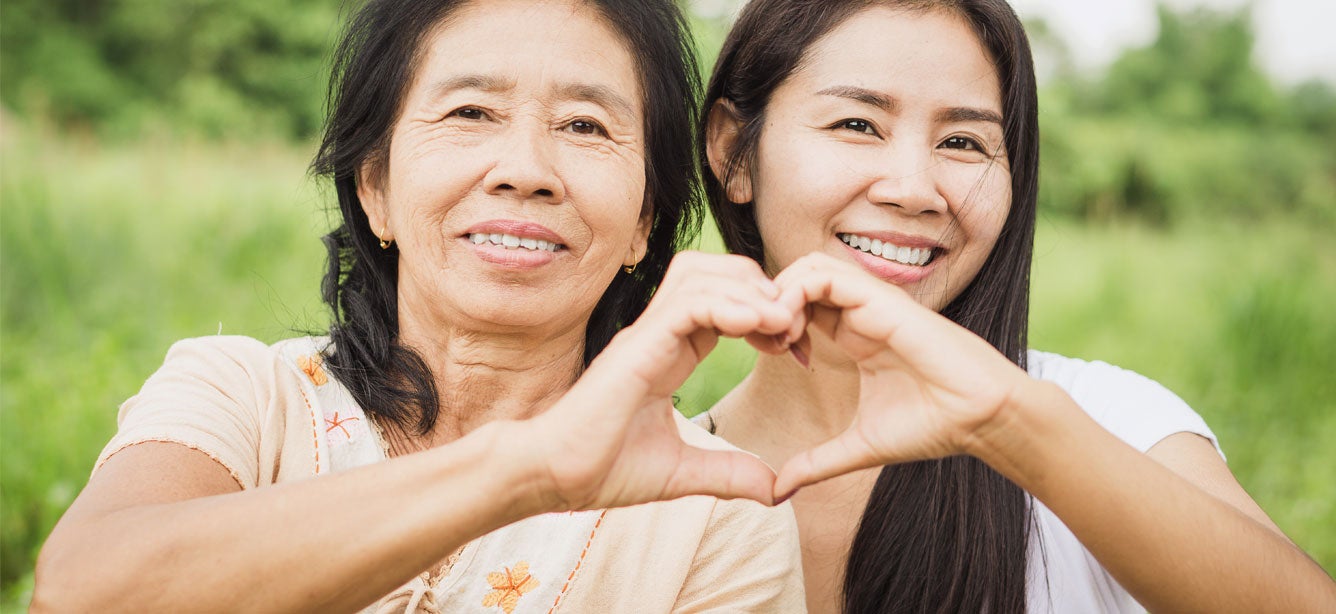 A senior Asian mom is making a heart shape with her hand and her daughter's hand.