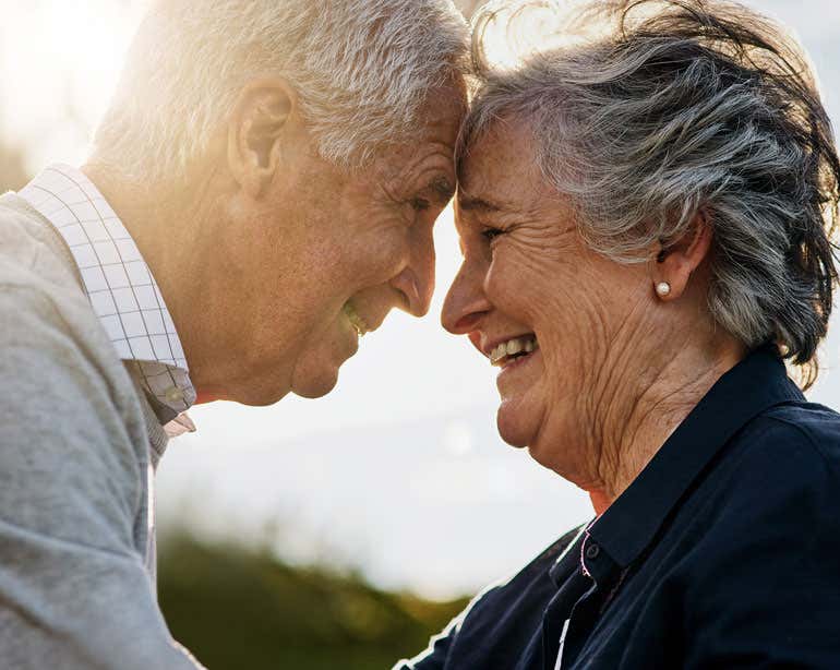 A happy senior Caucasian couple embrace each other, forehead to forehead, while enjoying the outdoors.