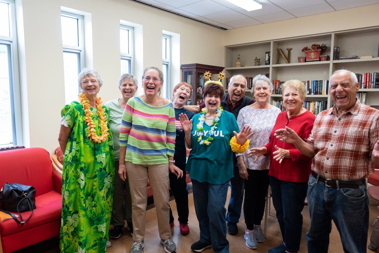 A cheerful group of older adults poses together, smiling and laughing in a community room.