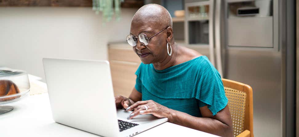 A senior Black female is using her laptop at her kitchen table, thinking about how to create a great password for her email.