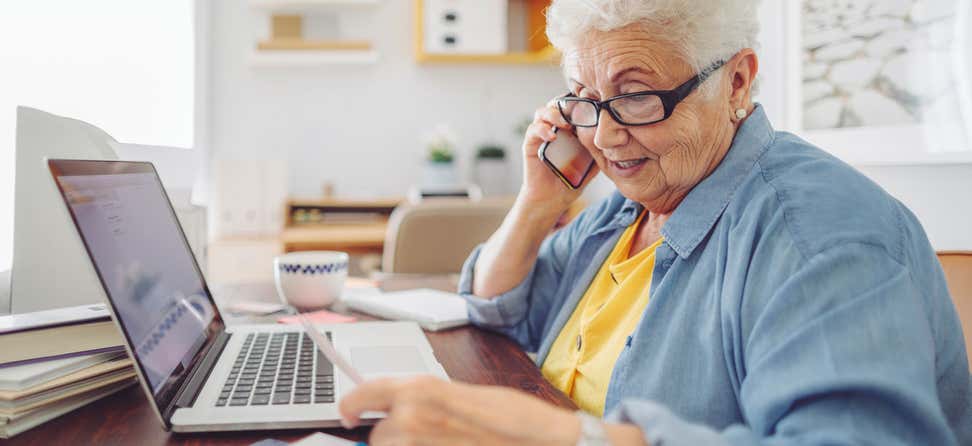 A senior woman is managing her finances as she sits at her kitchen table.