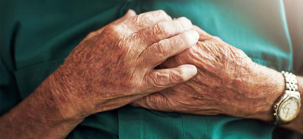 A close up shot of a senior man's hands placed over his heart, as if he's in pain.
