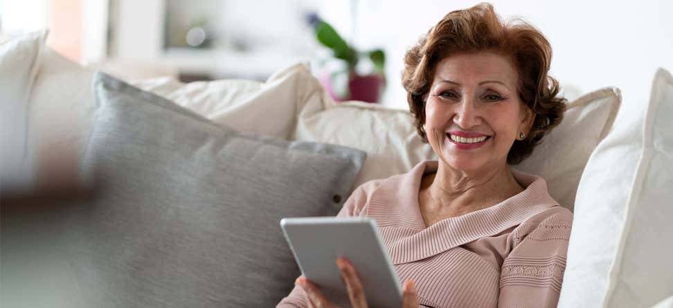 Older Hispanic/Latina woman on couch with tablet.